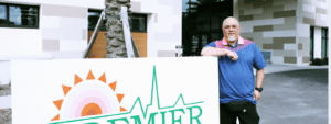 Jason Kalua standing next to Premier Community Healthcare sign